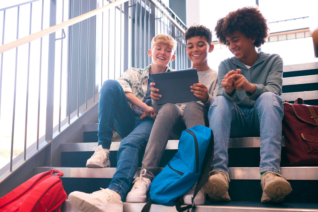 Drei Jungs sitzen auf einer Treppe, der mittlere Junge hat ein Tablet in der Hand