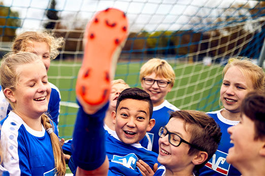 Eine Kinder-Fußballmannschaft in Volksbank-Trikots feiert einen Torschützen