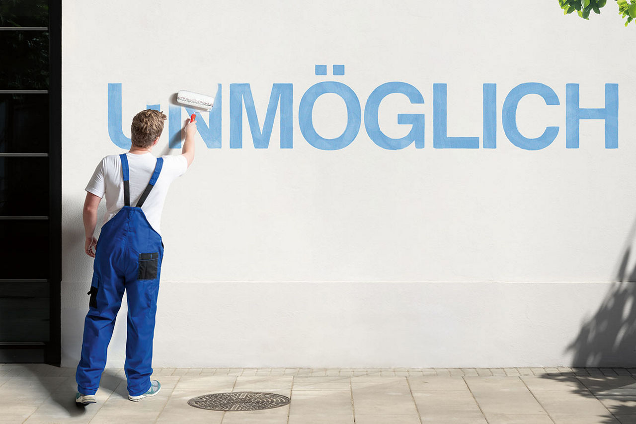 Junger Mann in Latzhose übermalt den Schriftzug „Unmöglich“ auf einer Wand